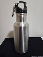 Full front view of the stainless steel water bottle showing the body and black lid with carabiner.