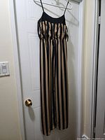 Full view of the new long striped dress on a hanger, showing vertical beige and black stripes, thin spaghetti straps, and long flowing length.