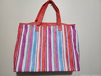 Full front view of handbag showing multicolor vertical stripes in fabric with red faux leather handles and trim
