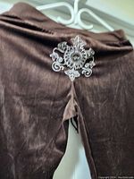 Close-up of brown velvet pants showing embroidered decorative detail on back waistband.