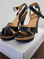 Pair of black patent leather open toe high heel shoes on white original box, angled front and side views.