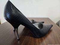 Side view of one black faux snakeskin texture high heel showing metallic thin heel and pointed toe
