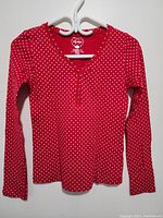 Full front view of the red long sleeve top with white polka dots, hung on a hanger