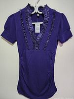 Front view of purple decorative silk top with V neckline and ruffled trim, on hanger