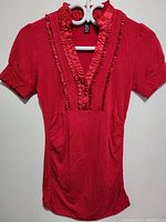 Front view of the red silk top showing full garment, puff sleeves, pockets, and ruffled neckline details.