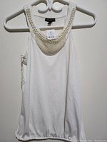 Front view of white sleeveless top on hanger showing decorative pearl collar and elastic hem.