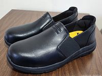 Side angle view of pair of new black Dakota WorkPro series work shoes on wooden surface showing the side, elastic inserts, and sole