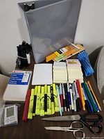 Overview of the office supplies laid out on a wooden surface including binder, writing instruments, sticky notes, and scissors.