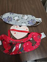 Two sleeping masks laid out on a dark wood surface, clearly showing fabric patterns and elastic straps.