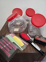 Four clear plastic containers with red lids along with grooming tools displayed on a table.
