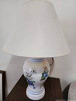 Full view of the porcelain floral table lamp with white fabric shade showing overall shape and design.