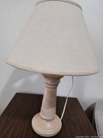 Full view of the table lamp showing the wood turned base and tapered fabric shade on a dark surface.