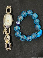 Photo showing Timex women's wristwatch and blue beaded bracelet side by side on black background.