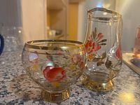 Two crystal glass items, including a goblet and a creamer jug, placed on a kitchen countertop. Both feature hand-painted floral artwork and gold detailing.