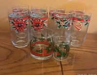 Photo of six collectible glass cups with Christmas poinsettia and holly decorations arranged on a wooden surface.