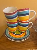 Four colorful striped ceramic teacups stacked inside each other on matching striped plates on a wooden surface.