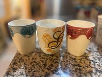 Three teacups with rose designs placed side by side on a granite countertop in soft lighting.