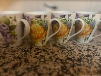 Front angle showing five ceramic teacups with multicolored floral patterns of yellow and purple flowers on a white background, arranged side-by-side.
