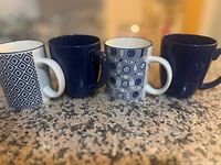 Photo of four ceramic teacups with two white and blue patterned and two solid blue designs, arranged on a speckled countertop.