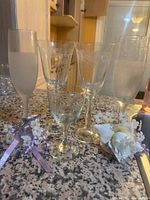 Photo shows six delicate glasses on countertop, including two frosted champagnes flutes, two etched wine glasses, one smaller etched glass, and one clear wine glass, with floral decorations placed nearby.