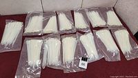 Thirteen packages of white zip ties, each package sealed, all laid out flat for inventory.