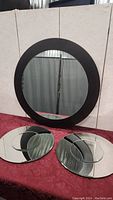 Three round mirrors on red fabric, one large with black frame and two smaller frameless with curved glass accent