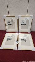 Four new Ikea gold photo frames with white mats, each 12x16 inches, with original labels and protective corners visible.
