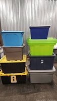 Full view showing stack of eight assorted colored plastic storage totes in various sizes and lids