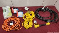 Full lot image with extension cords of different colors and power bars, showing new and used items on red surface