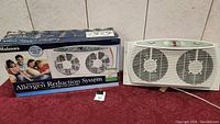 Holmes twin window fan alongside its original box featuring allergen reduction system description and product image.