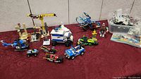 Image showing entire lot of Lego vehicles and structures arranged on a red surface, including jeep, police truck, motorbikes, helicopter, crane, figures and parts bin.