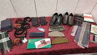 Full lot overview showing men's shoes, scarves, belts, gloves, ties, dresser valet and wallets on a red tablecloth.