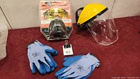 Photo showing safety combo kit box, face shield with yellow headband, and two pairs of work gloves laid out on a surface.