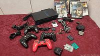 Full lot overview showing PS2 console, four controllers (three black, one red), four game cases, various cables, memory cards, and multitap adapter all laid out on red background.