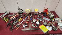 Wide view of assorted tools on red cloth including hammers, pliers, chisels, measuring tools, and power tool accessories.