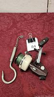 Overall view of vintage Zebco Cardinal 6X fishing reel with green line and metal fishing hook on red fabric background.