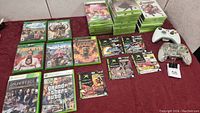 Display of Xbox 360 and Xbox One games laid out including Far Cry, GTA IV, Injustice games and two Xbox controllers (one white wireless and one transparent wired).