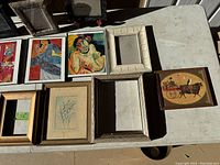 Top view showing collection of colorful abstract artworks and vintage style art, alongside empty frames arranged on a table