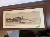 Front view of framed pencil seaside sketch showing coastal houses, a lighthouse, boats and shoreline in a horizontal composition.
