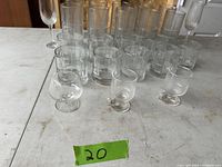 Angle showing 26 assorted clear drinking glasses including tumblers and three smaller brandy glasses in front
