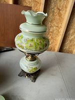 Side angle showing lamp's pale green ceramic body with yellow and white floral decoration and ornate metal feet base