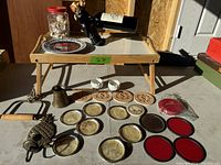Photo of wooden bed tray with abalone shell coasters, brass and metal holders, red and brown coasters, and small white dishes.