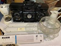 Overview of party items including Sony stereo, punch bowl with cups, white ceramic teapot, and coffee thermos with fluorescent light fixtures in foreground.