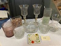 Photo showing two tall glass goblets with twisted stems, three clear cut glass bowls, pink tumbler, two clear rectangular glass vases with beads, clear flared glass vase, and small floral ceramic dish.