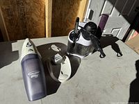 Overview image showing Black & Decker Dust Buster handheld vacuum with charger next to black hair dryer and purple styling tools on white organizer stand.