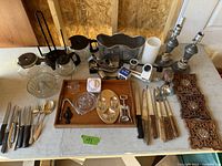 Image showing a variety of household items including knives, lamps, cutlery, wooden panels, and kitchen utensils arranged on a white table.