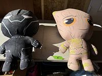 Two inflatable plush toys, Black Panther and Groot, side by side on a surface showing front and back views.