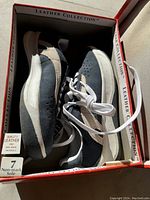 Photo of pair of new leather sneakers inside open box, visible size 7 label, showing both shoes laid flat in the box with lace tied.