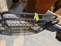 Black metal bed frame shown folded, displaying coil spring support and tubular metal construction.