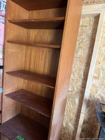 Full view inside wooden bookcase with five shelves, showing dust needing cleaning.